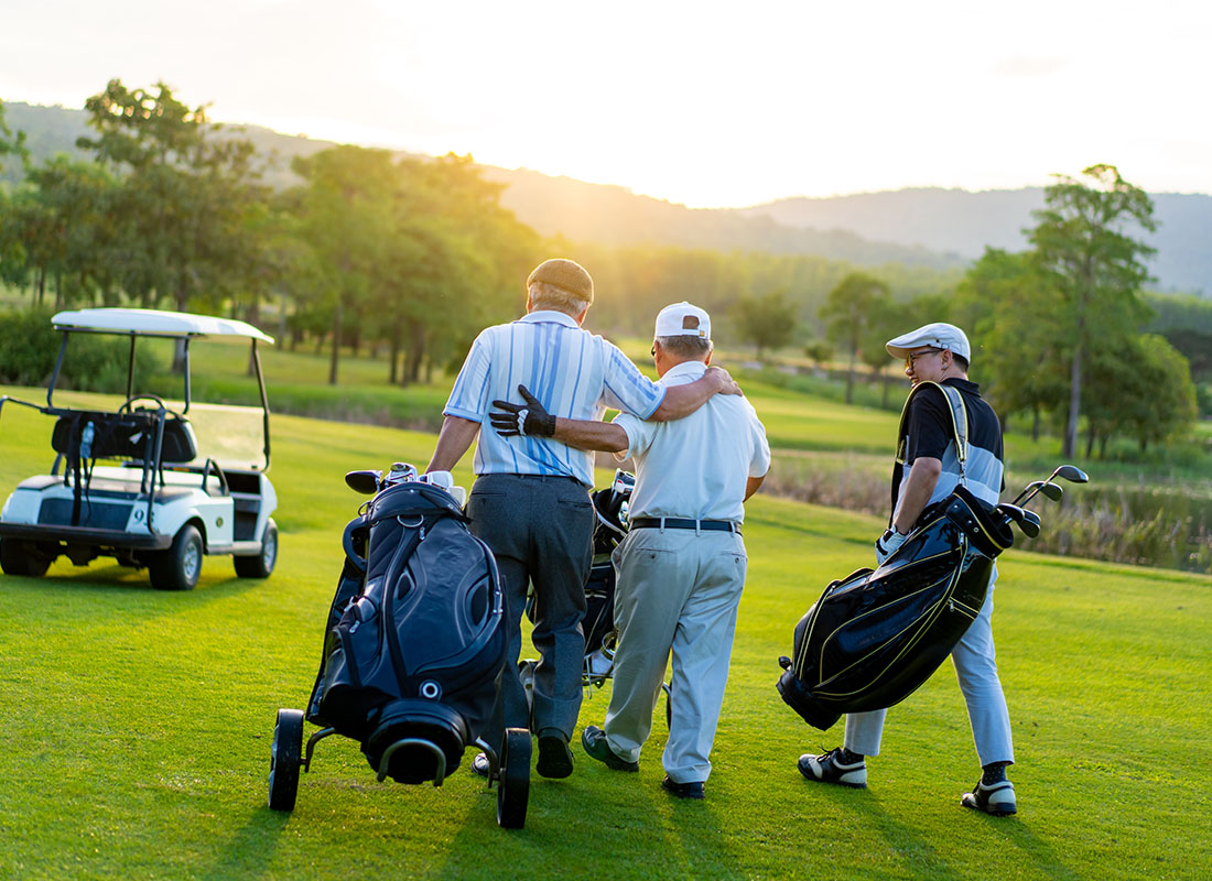 Golf Insurance Landing - Rear View of Three Businessmen Walking on a Green FIeld at a Golf Course Holding Equipment Ready to Play