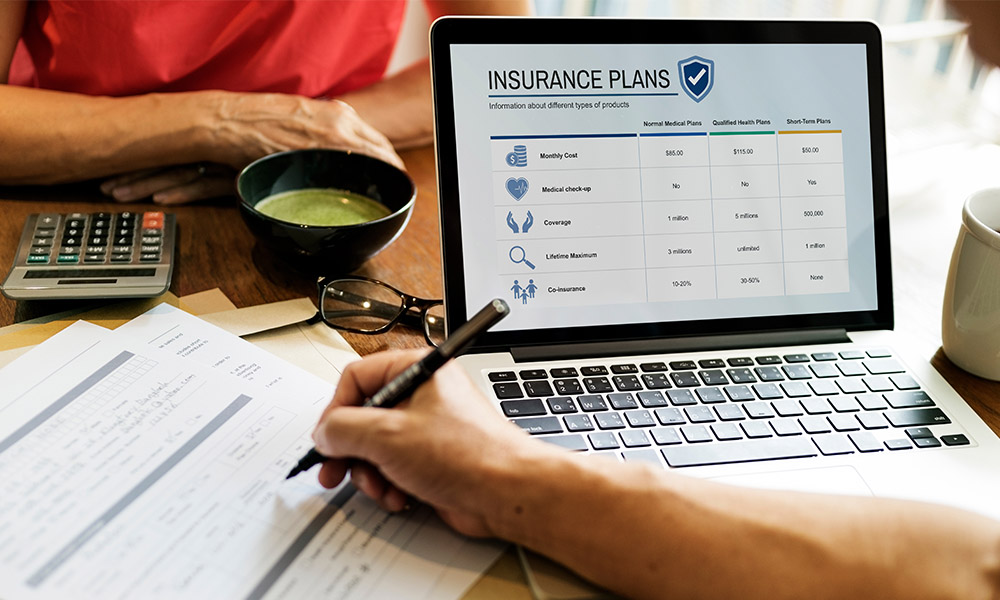 Blog - Person Filling Out Forms with Laptop Open in Front of Them on a Page that Lists Insurance Plans